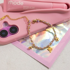 Detail of gold chain bracelet with purple woven rope, flower and leaf charms on pink background