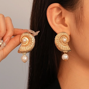 Close-up of gold conch shell earrings with white pearls worn by a model in profile