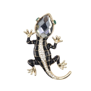 Detailed macro view of a gold-plated gecko brooch with black enamel and smoky grey crystal