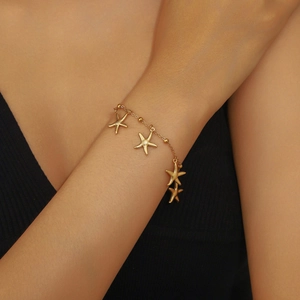 Detailed close-up of golden starfish pendant bracelet worn on wrist with delicate beads