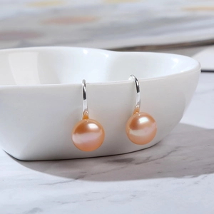 Detail of pink natural pearl drop earrings hanging on a white heart-shaped ceramic bowl
