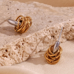 Two-tone intertwined stainless steel C-shaped hoop earrings on a stone surface