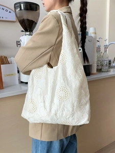 White embroidered canvas tote bag with floral patterns worn by a model in a cozy cafe setting