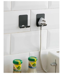 Detail of black U-shaped metal adhesive hooks holding power plugs on a white tiled wall