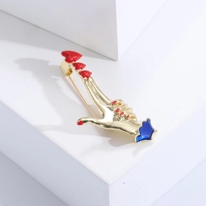 Creative gold heart-shaped hand gesture brooch with red enamel on a white geometric background