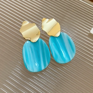 Detail of irregular gold metal earrings with blue marble resin oval drop charms