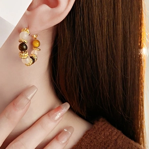 Detail of round tiger eye stone earring with gold plating and silver needles on model