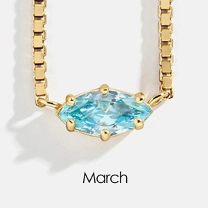 Macro shot of gold necklace featuring marquise-cut light blue March birthstone charm