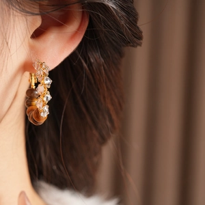 Close-up of C-shaped gold hoops with clear crystals and tiger eye beads on model