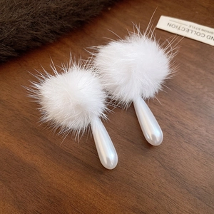Close-up of white plush pom-pom earrings with faux pearl drops on a wooden background