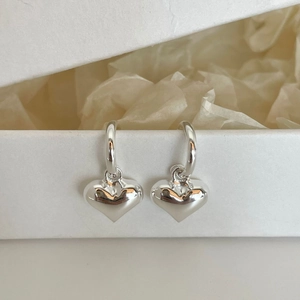 Detailed view of 925 silver heart stud earrings hanging on a white minimalist gift box