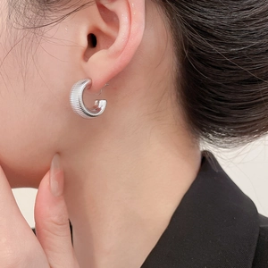 Macro shot of silver C-shaped threaded stud earrings with a polished metallic texture