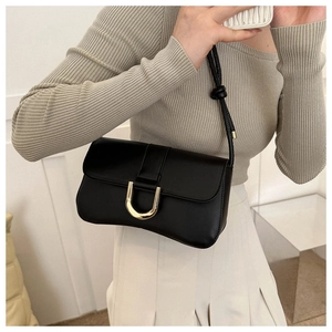 Detail of black faux leather underarm bag featuring a gold U-shaped buckle and knotted strap