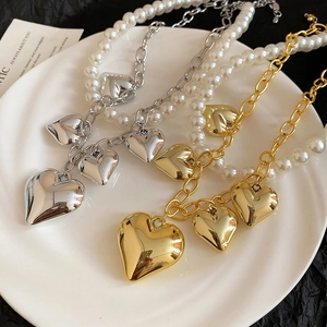 Detail of heart pendants on hybrid pearl and metal chain in gold and silver finishes