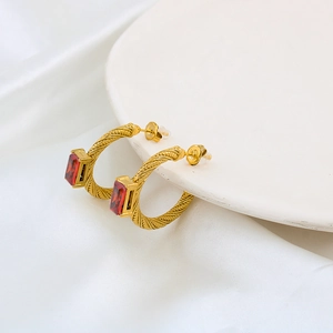 Macro shot of gold C-shaped twisted earrings with red rectangular stones on silk