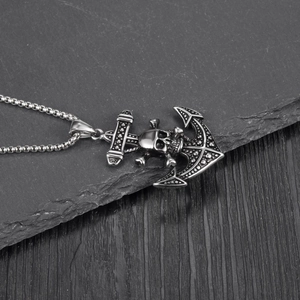 Retro stainless steel anchor skull pendant on box chain over dark slate and wood background