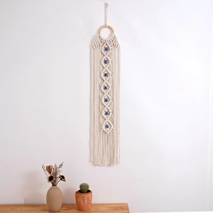 Detail of woven cotton macrame wall hanging featuring blue evil eye beads and tassels