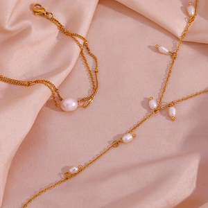 Gros plan d'un collier en Y doré avec perles baroques blanches sur soie rose