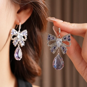 Close-up of elegant bow earrings with purple teardrop crystals and sparkling zircons