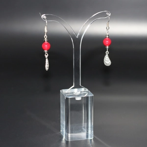 Elegant red bead and silver drop earrings displayed on a clear acrylic jewelry stand