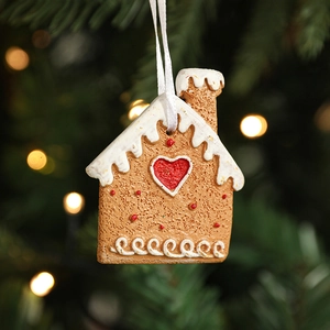 Gingerbread house Christmas tree ornament with red heart hanging on a festive pine branch