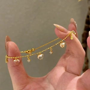 Detailed view of a gold heart pendant bracelet with tassels and crystal accents