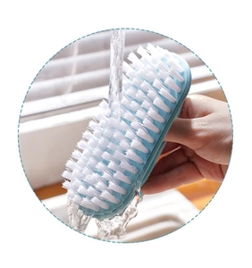 Close-up of blue cleaning brush with soft white bristles being rinsed under a faucet