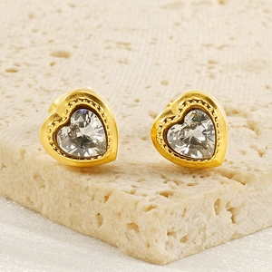 Dettaglio di orecchini a cuore dorati con zircone centrale e bordo con perline
