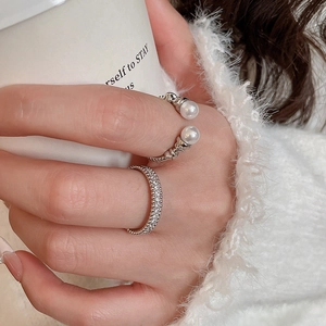 Close-up of zircon stacked rings and pearl open ring on hand with coffee cup