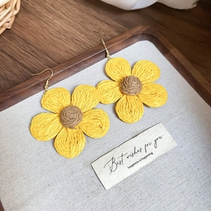 Detail shot of yellow sunflower resin weave earrings on a rustic wooden display