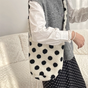 Detail of white plush lamb wool bucket bag with large black polka dots on a shoulder strap