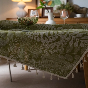 Detail of olive green linen tablecloth with white leaf patterns and fringe edges