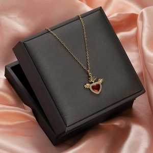 Close-up of golden necklace with winged red heart pendant on premium black jewelry box