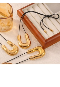 Detail view of large gold U-shaped pendants on black leather cords against a warm backdrop