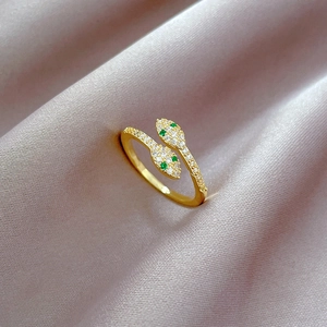 Macro detail of gold snake ring with green gem eyes and white zircon inlay on purple silk