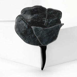 Detail of a black acrylic rose brooch with gold glitter finish on a white surface