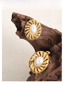 Détail d'une boucle d'oreille spirale dorée avec perle blanche et strass brillants