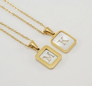 Macro view of 18K gold plated stainless steel square pendants with shell inlay and letters