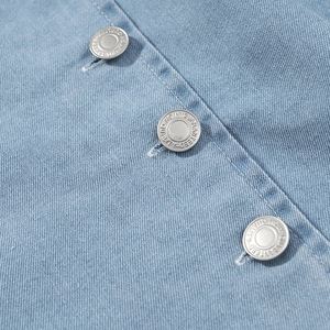 Nahaufnahme von silbernen Metallknöpfen auf hellblauem Jeanskleid mit Köperstruktur