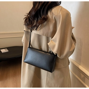Detail view of a minimalist black leather baguette bag on a model wearing an elegant trench coat