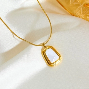 Gros plan d'un collier doré avec pendentif rectangulaire blanc sur tissu en soie blanche