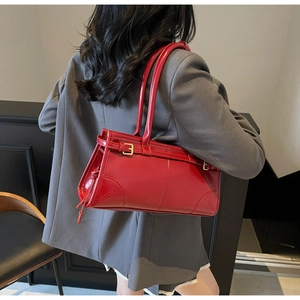 Chic red faux leather shoulder bag with gold hardware shown on a female model in a grey suit