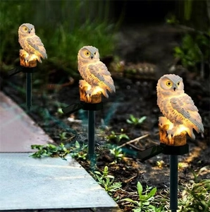 Three solar owl garden lights with resin stumps glowing with warm LED light in a garden
