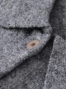 Dettaglio del colletto polo in maglia grigia con bottone marrone e trama fine