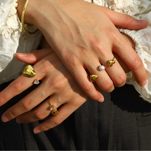 Close-up of gold heart rings with pearls and zircon on hands with lace background