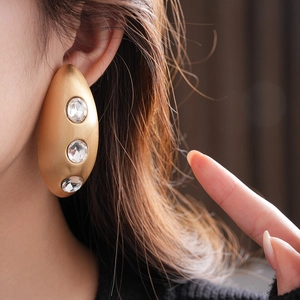 Close-up of golden matte oval earrings with sparkling rhinestones on model's ear