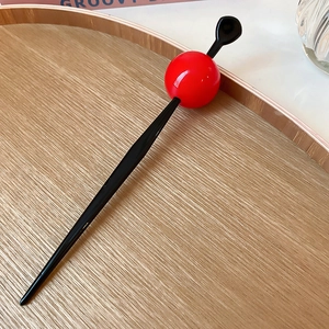 Detail of a minimalist hair stick with a polished red ball on a light wood tray