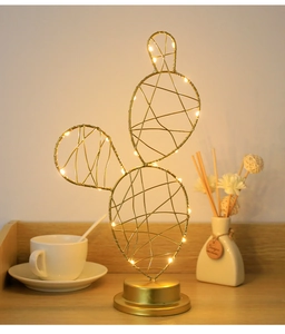 Close-up of golden metal cactus desk lamp with warm LED lights on wooden table