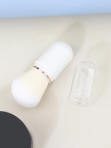 Macro view of portable retractable powder brush with soft white bristles and capsule case