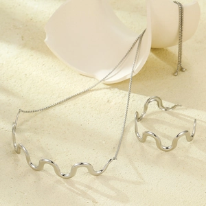 Polished silver wavy necklace and cuff bracelet set on a textured stone surface